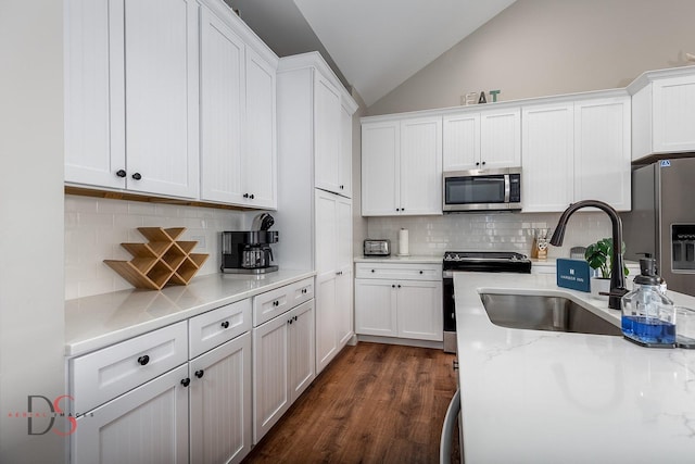 kitchen with backsplash, stainless steel appliances, vaulted ceiling, dark wood-type flooring, and white cabinetry