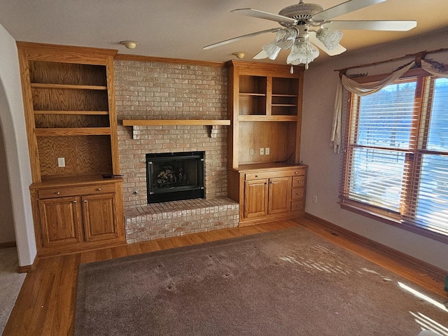 unfurnished living room featuring hardwood / wood-style flooring, ceiling fan, ornamental molding, and a fireplace