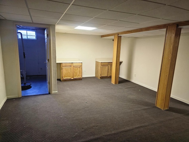 basement featuring a paneled ceiling and dark carpet