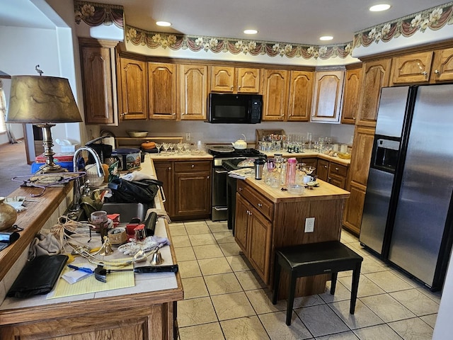 kitchen with a center island, sink, stainless steel refrigerator with ice dispenser, light tile patterned floors, and range