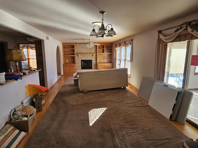 living room featuring hardwood / wood-style floors, built in shelves, ceiling fan with notable chandelier, and a brick fireplace