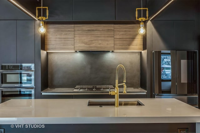 kitchen with an island with sink, multiple ovens, stainless steel fridge, and decorative light fixtures