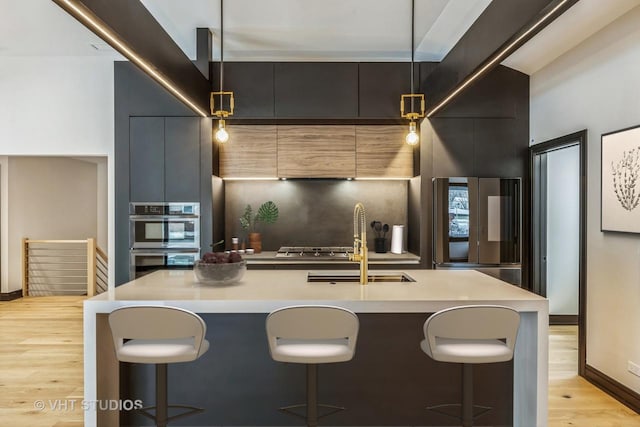 kitchen with stainless steel appliances, an island with sink, a kitchen breakfast bar, and decorative light fixtures