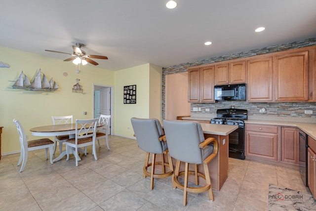 kitchen featuring a center island, black appliances, ceiling fan, decorative backsplash, and a breakfast bar area