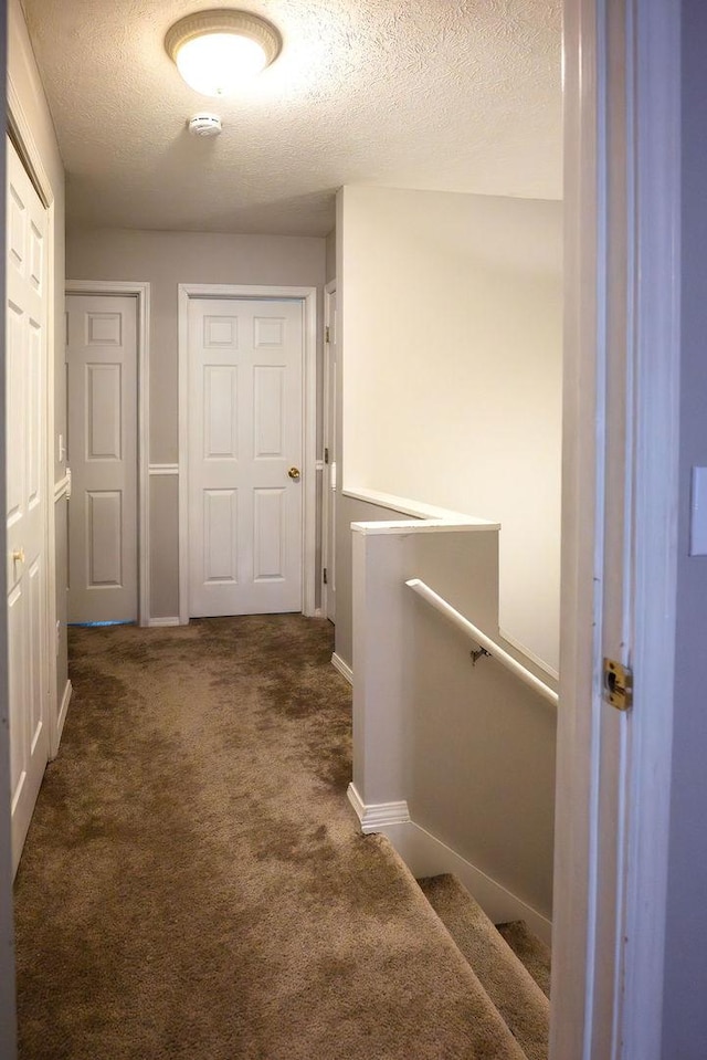 hall featuring dark colored carpet and a textured ceiling