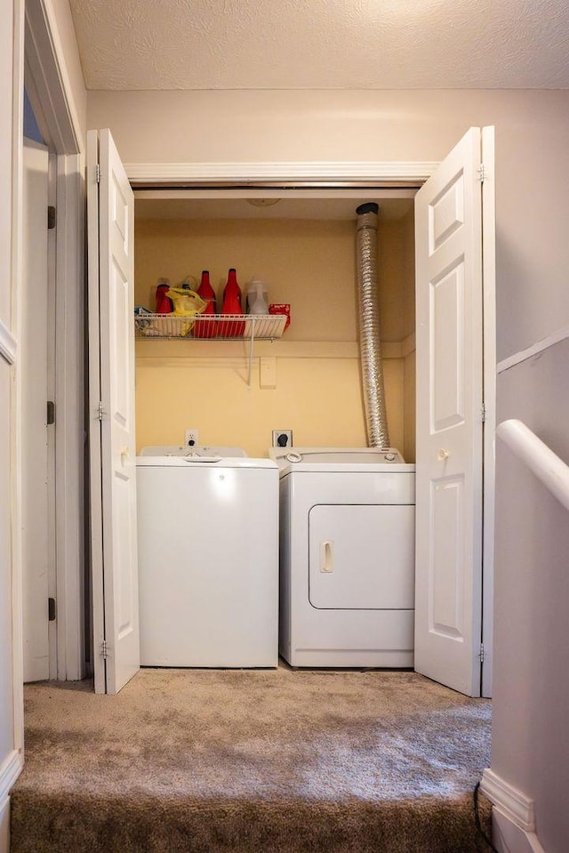 clothes washing area with washing machine and dryer, light colored carpet, and a textured ceiling