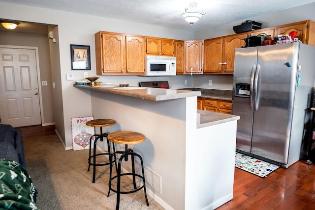 kitchen featuring kitchen peninsula, stainless steel fridge, hardwood / wood-style floors, a kitchen bar, and range