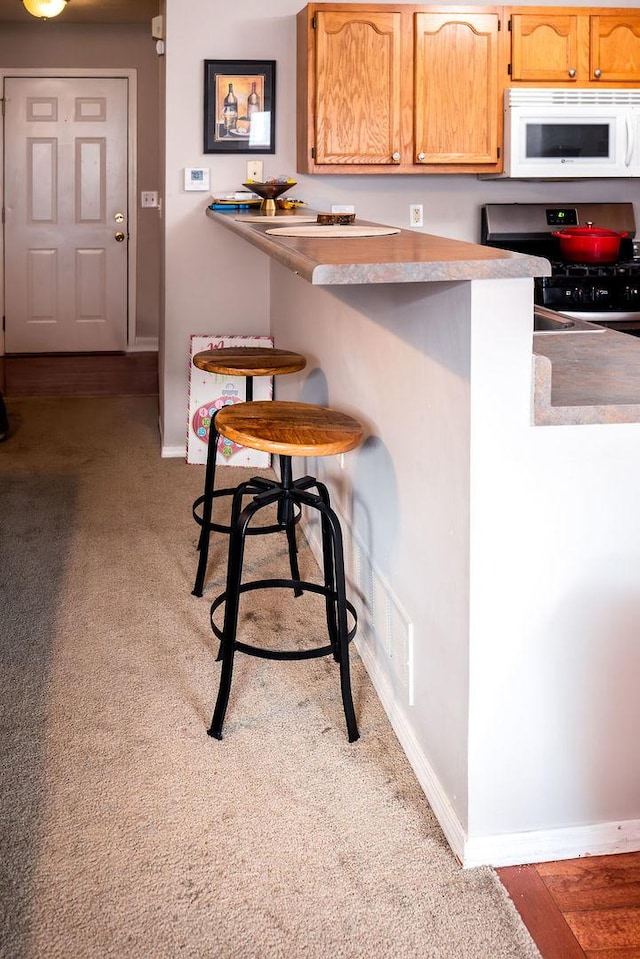 kitchen featuring a breakfast bar, light colored carpet, kitchen peninsula, and stainless steel range with electric cooktop