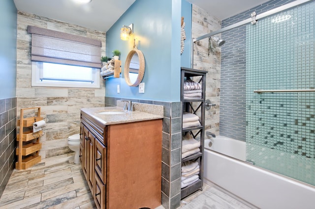 full bathroom with bath / shower combo with glass door, toilet, vanity, and tile walls