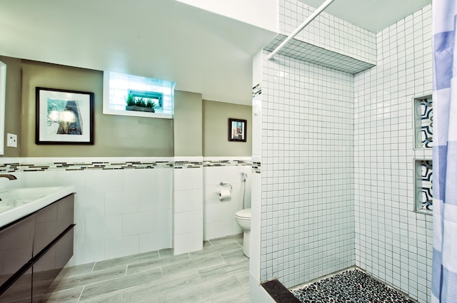 bathroom featuring toilet, vanity, tile walls, and a tile shower