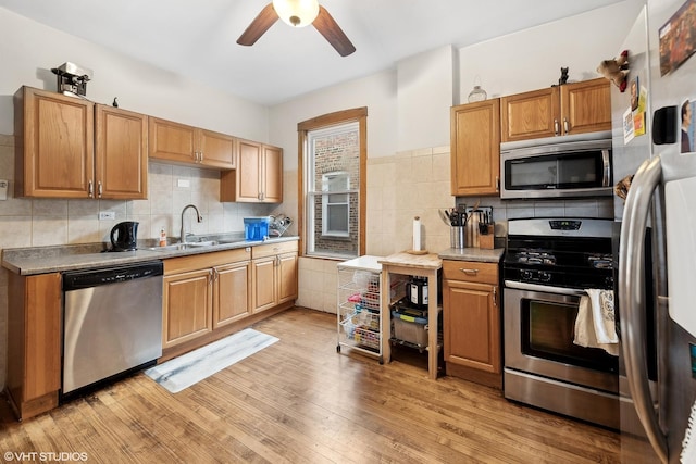 kitchen with appliances with stainless steel finishes, tasteful backsplash, sink, light wood-type flooring, and ceiling fan