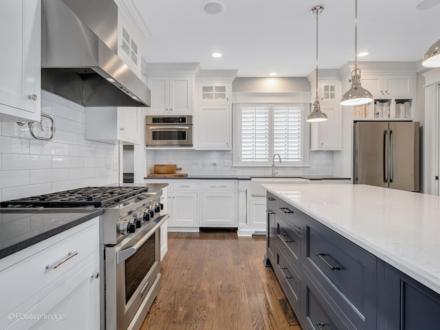 kitchen with pendant lighting, wall chimney range hood, white cabinets, and appliances with stainless steel finishes