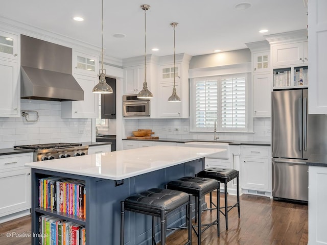 kitchen featuring appliances with stainless steel finishes, wall chimney exhaust hood, a center island, and white cabinets