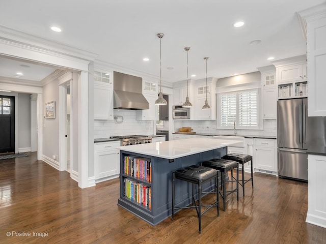 kitchen featuring stainless steel refrigerator, decorative light fixtures, white cabinets, a center island, and wall chimney range hood