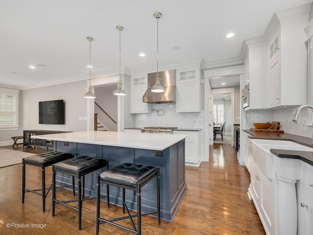 kitchen with white cabinetry, a breakfast bar, wall chimney exhaust hood, and a center island