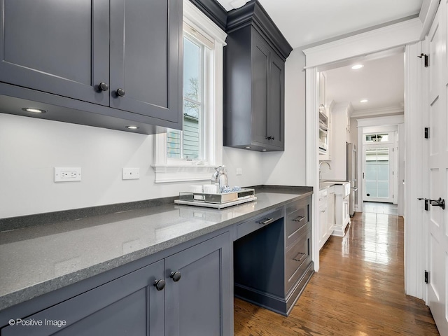 kitchen with gray cabinetry, ornamental molding, dark hardwood / wood-style flooring, and dark stone counters