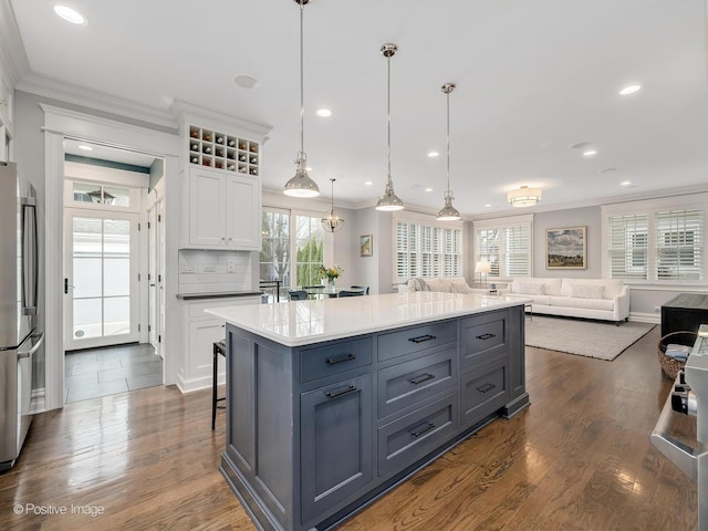 kitchen featuring pendant lighting, stainless steel refrigerator, white cabinetry, a center island, and crown molding