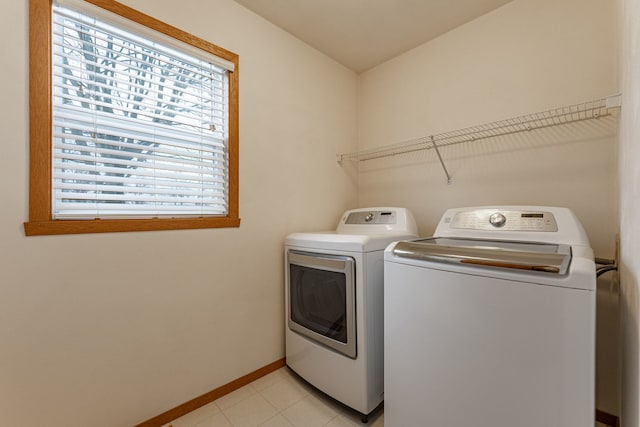 clothes washing area featuring laundry area, light tile patterned floors, baseboards, and washer and clothes dryer