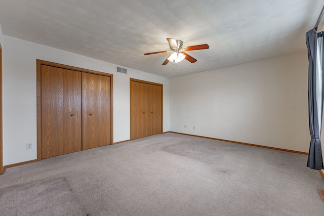 unfurnished bedroom with ceiling fan, light colored carpet, visible vents, baseboards, and multiple closets