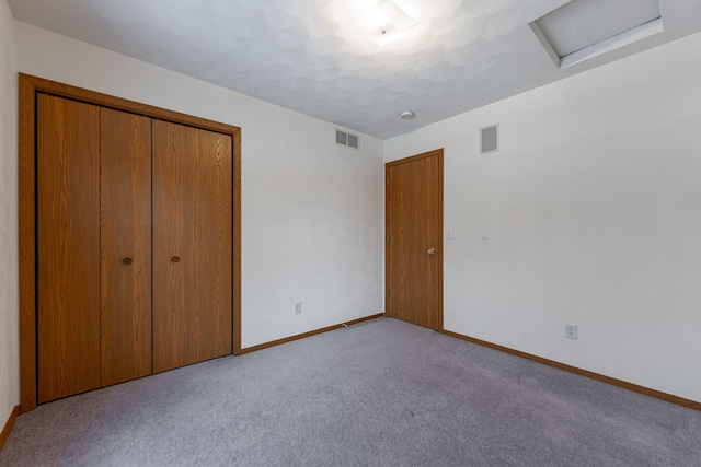 unfurnished bedroom featuring a closet, carpet flooring, visible vents, and attic access