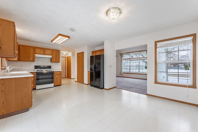 kitchen with light countertops, black fridge, brown cabinets, and white range with gas stovetop