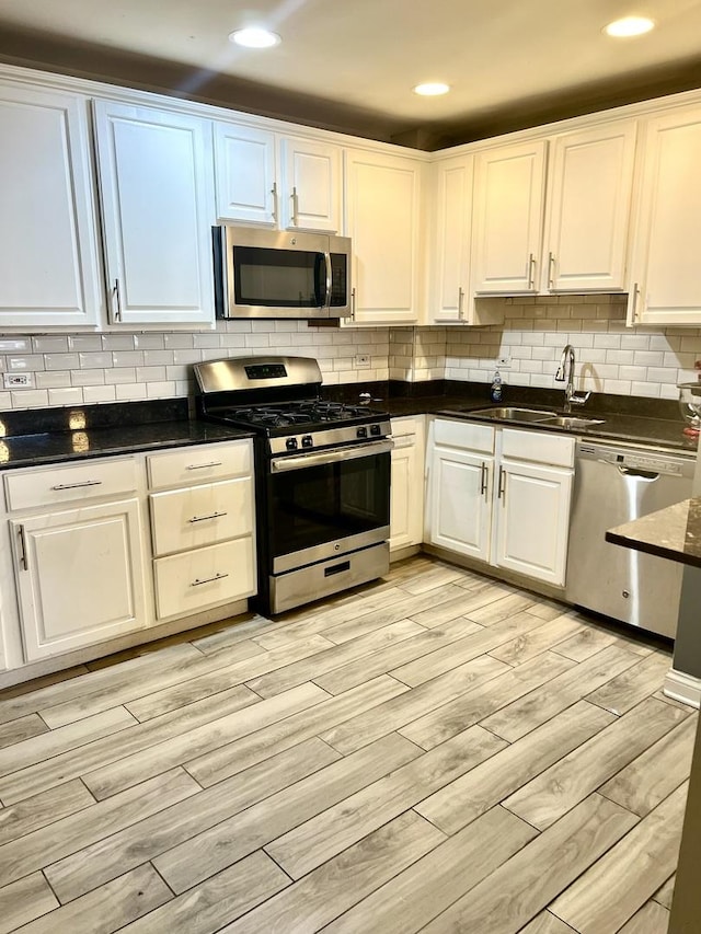 kitchen with appliances with stainless steel finishes, light hardwood / wood-style flooring, white cabinetry, and sink