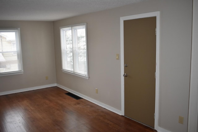 spare room featuring dark hardwood / wood-style flooring, a textured ceiling, and a wealth of natural light