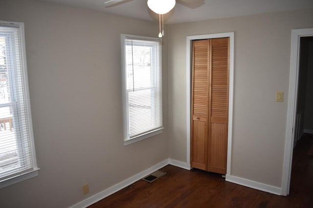 unfurnished bedroom with ceiling fan, dark hardwood / wood-style floors, a closet, and multiple windows