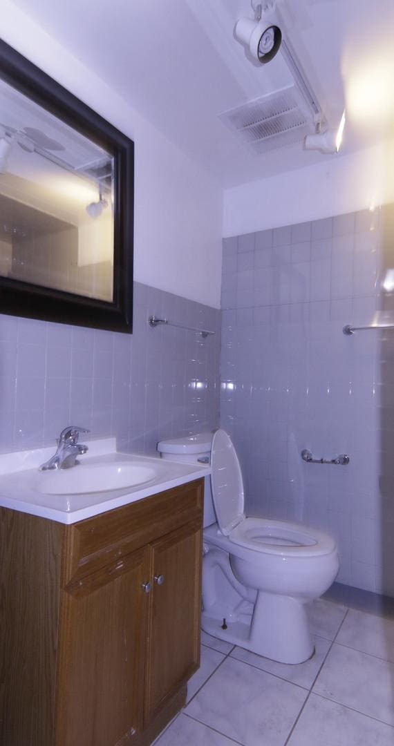 bathroom featuring toilet, tile patterned flooring, tile walls, and vanity