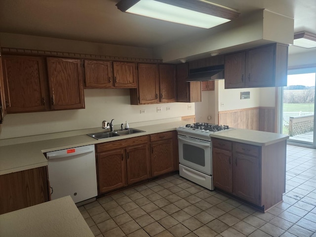 kitchen with white appliances, sink, wooden walls, range hood, and kitchen peninsula