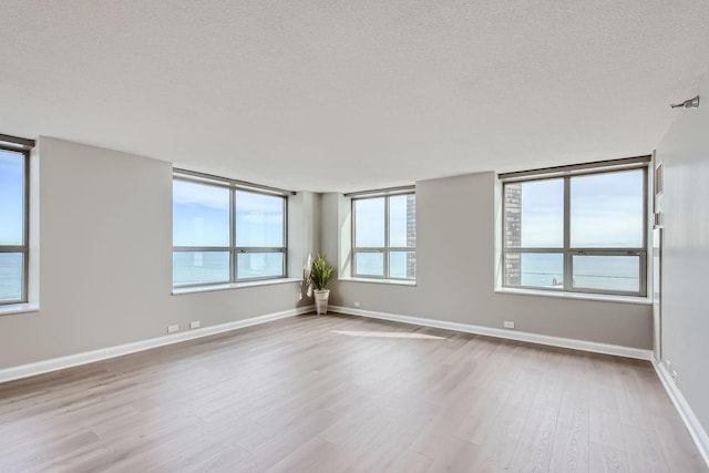 spare room featuring a water view, light hardwood / wood-style floors, and a textured ceiling