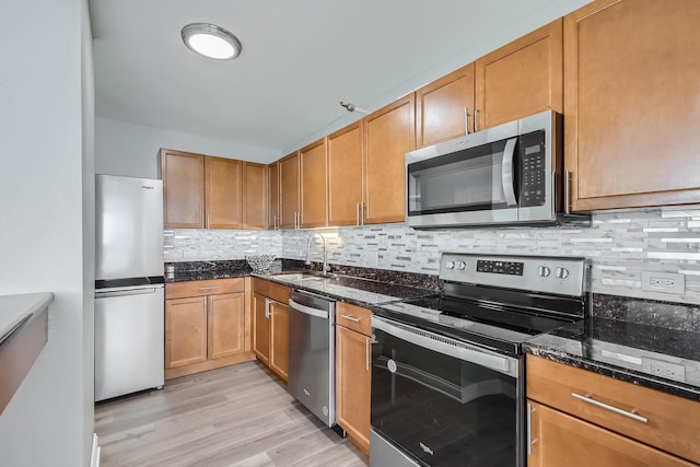 kitchen featuring backsplash, stainless steel appliances, sink, light hardwood / wood-style flooring, and dark stone countertops