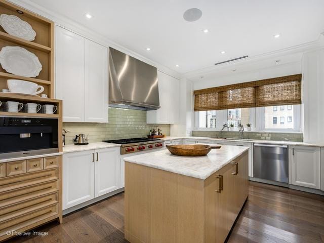 kitchen with appliances with stainless steel finishes, wall chimney exhaust hood, dark wood-type flooring, white cabinets, and a center island