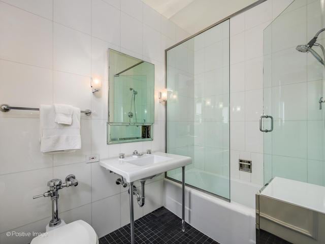 bathroom with toilet, shower / bath combination with glass door, and tile walls