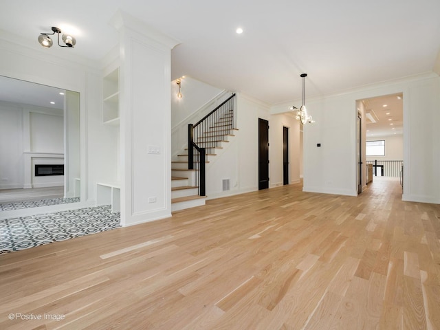 unfurnished living room featuring crown molding, light hardwood / wood-style flooring, and a notable chandelier