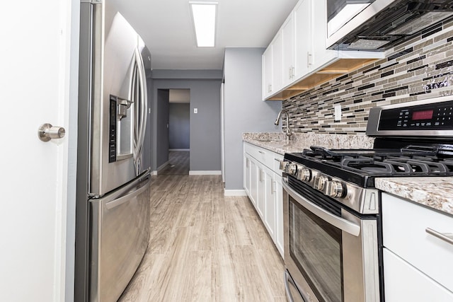 kitchen with tasteful backsplash, light stone counters, light hardwood / wood-style floors, white cabinets, and appliances with stainless steel finishes