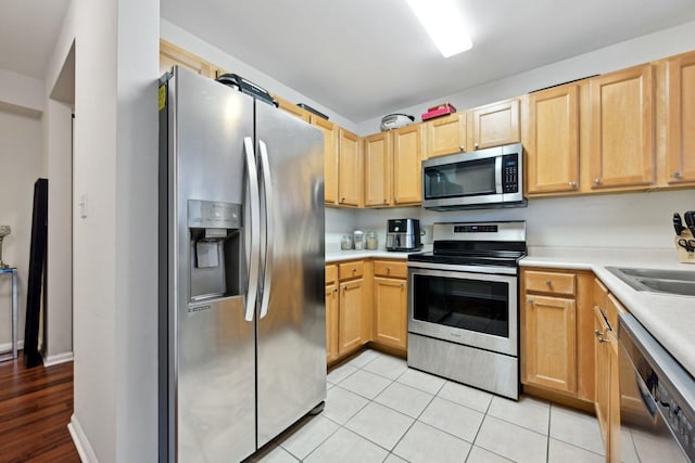 kitchen with light tile patterned floors, stainless steel appliances, light brown cabinetry, and sink