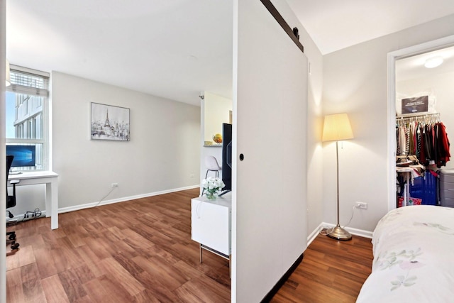 bedroom with a walk in closet, a barn door, hardwood / wood-style flooring, and a closet