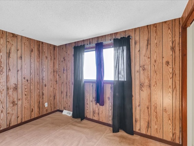 empty room featuring a textured ceiling and wood walls