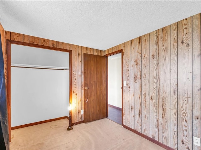 unfurnished bedroom with wood walls, light colored carpet, a textured ceiling, and a closet