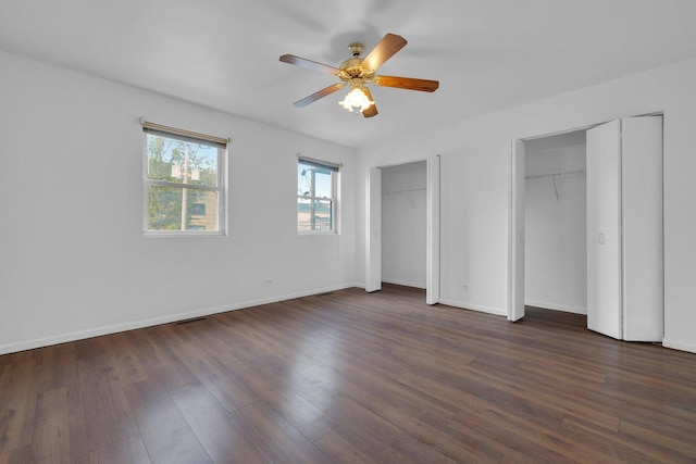 unfurnished bedroom featuring dark hardwood / wood-style flooring, ceiling fan, and multiple closets