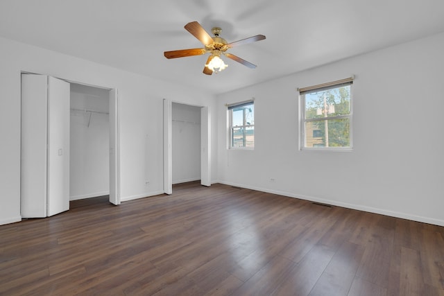 unfurnished bedroom with ceiling fan, dark hardwood / wood-style flooring, and two closets