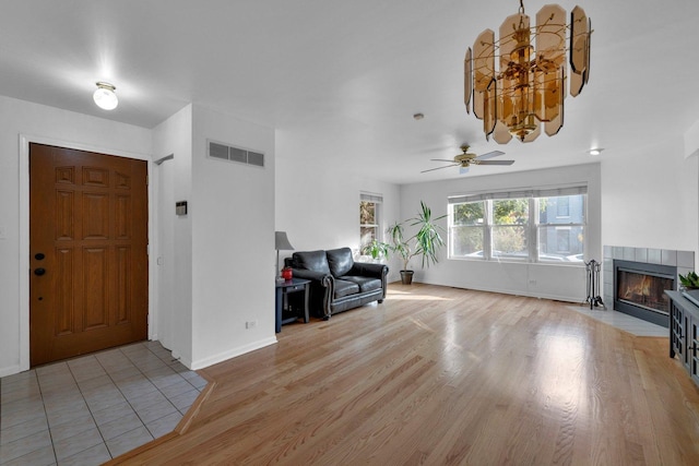 foyer featuring ceiling fan with notable chandelier, light hardwood / wood-style floors, and a tile fireplace