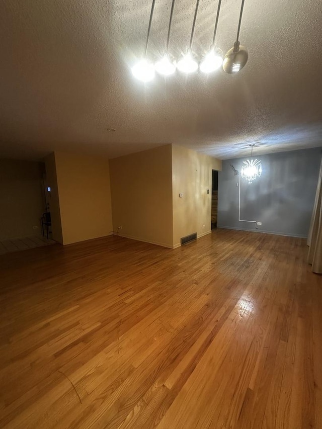 empty room with wood-type flooring, an inviting chandelier, and a textured ceiling