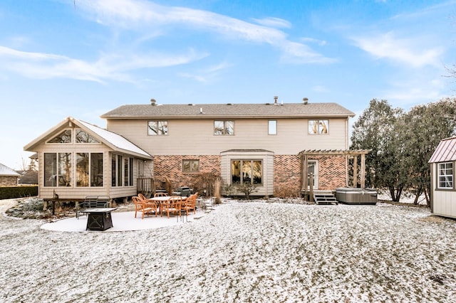 snow covered back of property with a pergola, a jacuzzi, a sunroom, and an outdoor fire pit