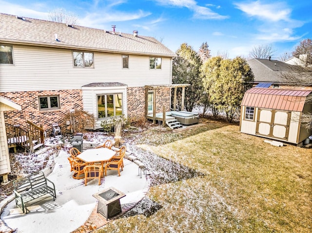 snow covered house with a patio, a fire pit, a storage unit, a yard, and a hot tub