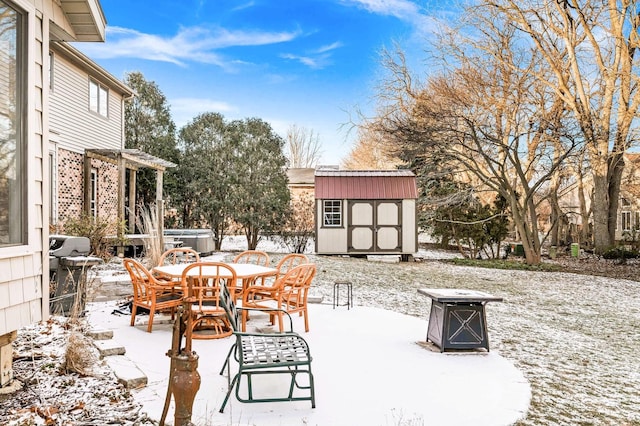 snow covered patio with a shed, a fire pit, and a hot tub