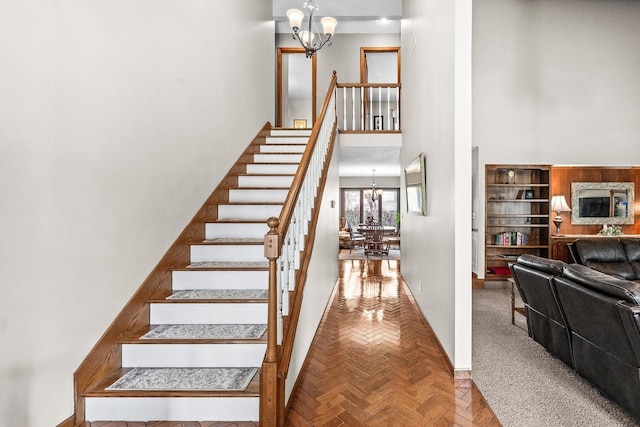 stairway featuring parquet flooring, a towering ceiling, and a chandelier