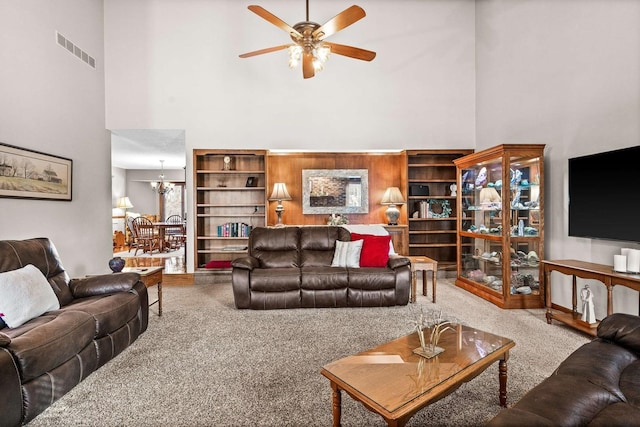 carpeted living room featuring a towering ceiling and ceiling fan with notable chandelier