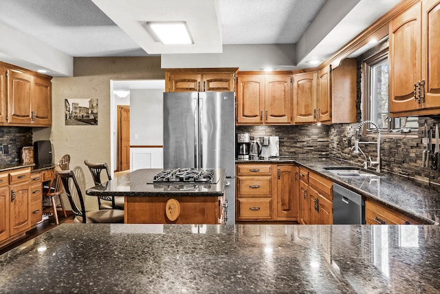 kitchen with appliances with stainless steel finishes, built in desk, tasteful backsplash, sink, and dark stone countertops